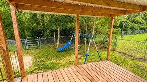 A wooden deck with a swing set and slide in the background. - Cozy Getaway in the heart of Ocala National Forest- in Salt Springs (Salt Springs)