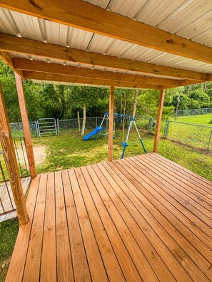 Een houten terras met een schommel en glijbaan op de achtergrond.