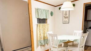 A compact kitchen with a refrigerator, a dining table with chairs, and a hanging light fixture. - Cozy Getaway in the heart of Ocala National Forest- in Salt Springs (Salt Springs)