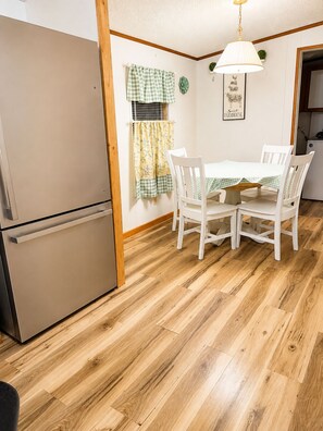 Een kleine keuken met een koelkast, een eettafel met stoelen en een hanglamp.