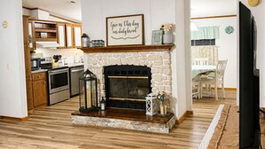 A living room with a fireplace, a television, and a kitchen in the background. - Cozy Getaway in the heart of Ocala National Forest- in Salt Springs (Salt Springs)