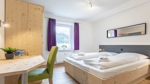 Une chambre à coucher avec un lit en bois, un bureau, une chaise et une fenêtre avec des rideaux.
