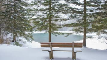 Eine hölzerne Bank in verschneiter Landschaft, im Hintergrund ein See und Bäume.