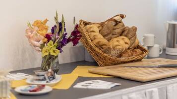 Ein Frühstücksbuffet mit einem Brotkorb, einem Blumenstrauß und einer Kaffeemaschine auf einem Tisch.