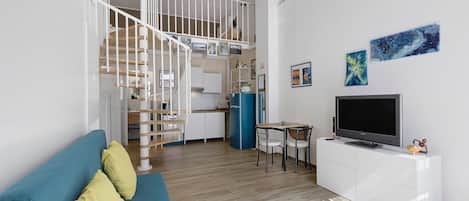 Un espacio habitable moderno con una escalera, una zona de comedor y un televisor sobre un mueble blanco.