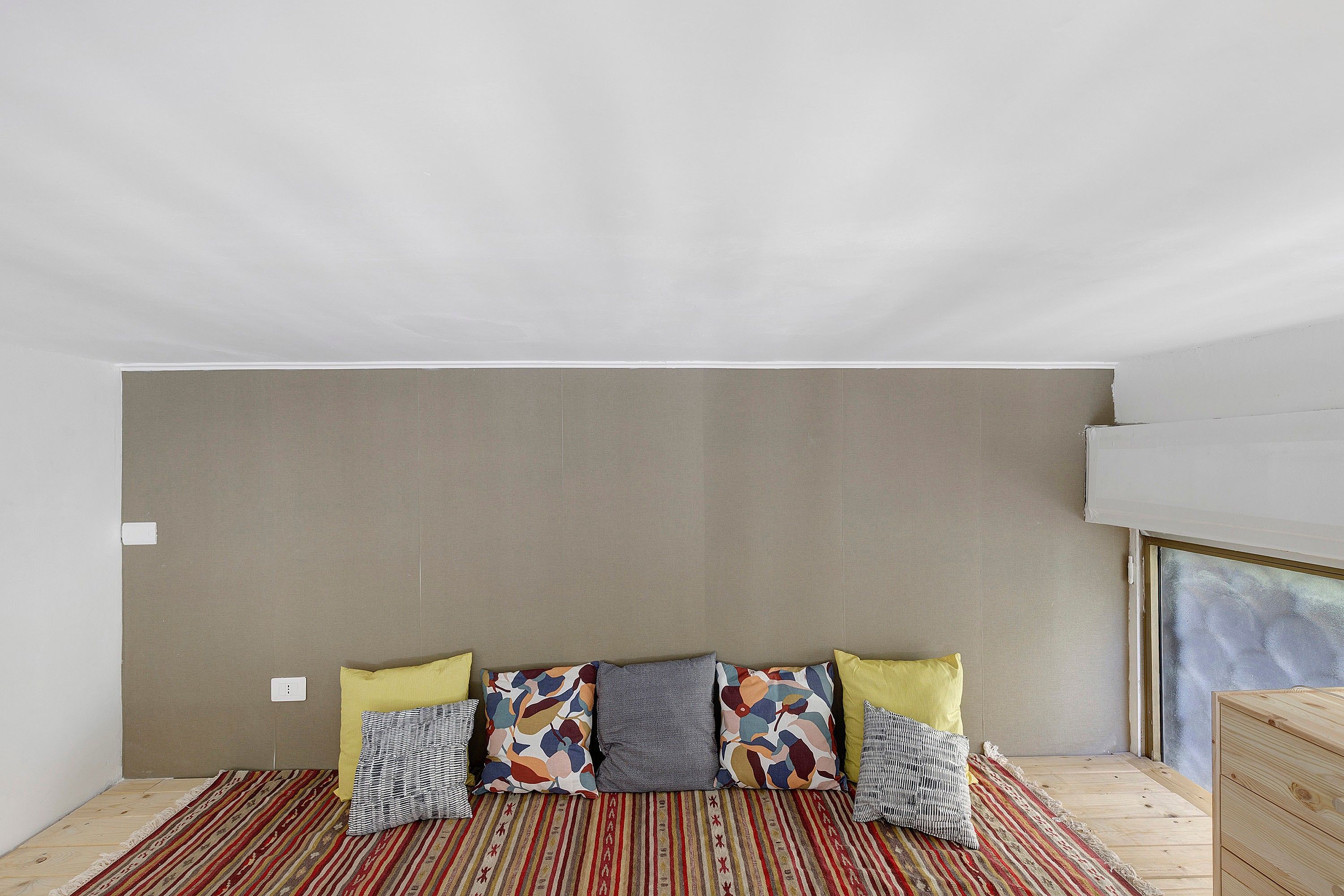 Une chambre avec une tête de lit de couleur neutre, un tapis à motifs et un plancher en bois.