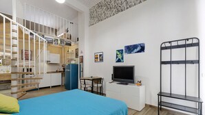 Quarto de hotel compacto com cama, escrivaninha com computador, televisão e beliche.