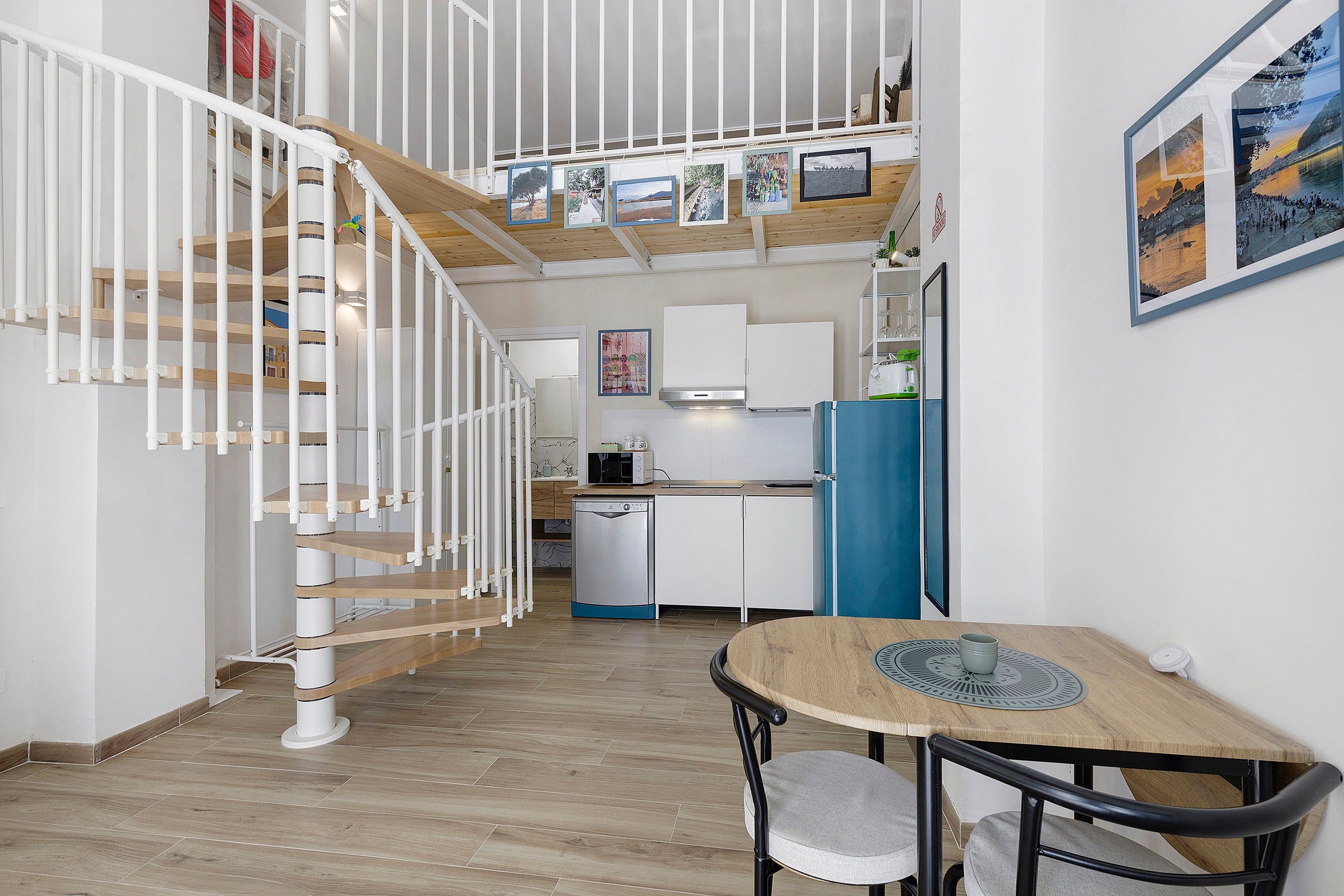 A modern kitchen with white cabinets, a blue refrigerator, and a dining area with a wooden table and chairs.