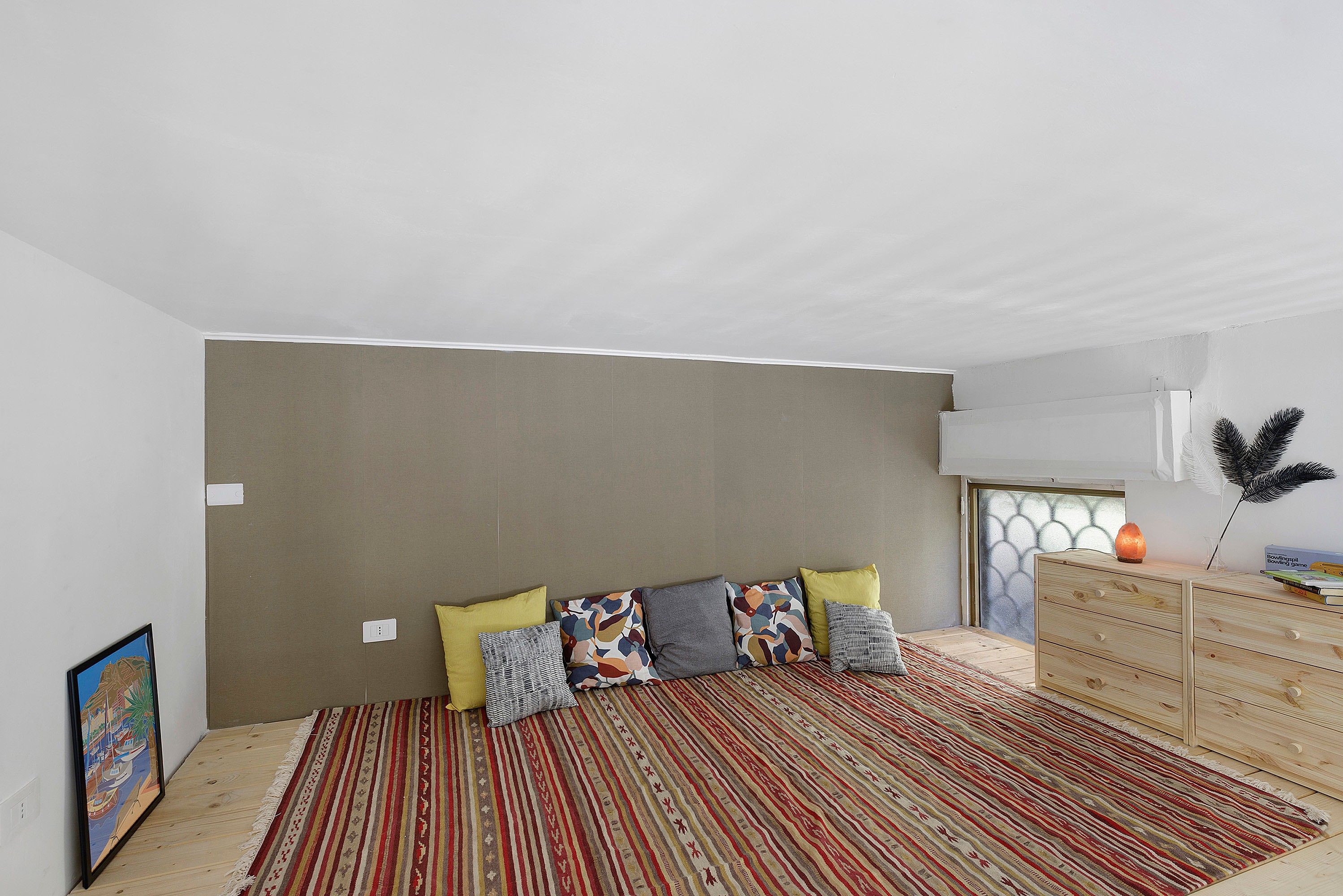 Une chambre à coucher avec un lit, une commode en bois, un tapis coloré et un tableau accroché au mur.