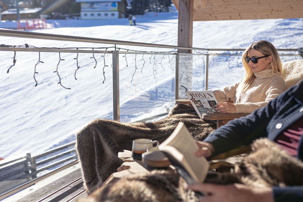 Una persona leyendo un libro en una mesa con vista a un paisaje nevado.