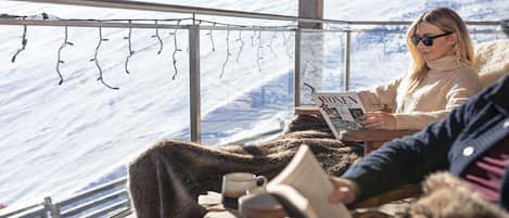 Una persona leyendo un libro en una mesa con vista a un paisaje nevado.