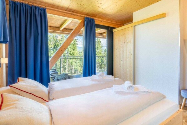 Una habitación con dos camas, cortinas azules y vista a árboles.