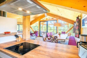 Una cocina moderna con una isla central, vigas de madera y una zona de comedor con sillas de colores.