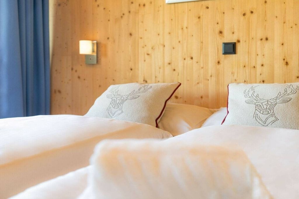 Una habitación de hotel con paredes de paneles de madera, dos camas con ropa blanca y una mesita de noche con lámpara.
