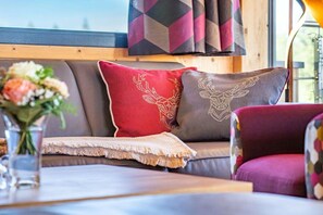 Ein gemütlicher Sitzbereich mit einer Couch, zwei dekorativen Kissen mit Tiermotiven, einer Vase mit Blumen und einem gemusterten Vorhang.