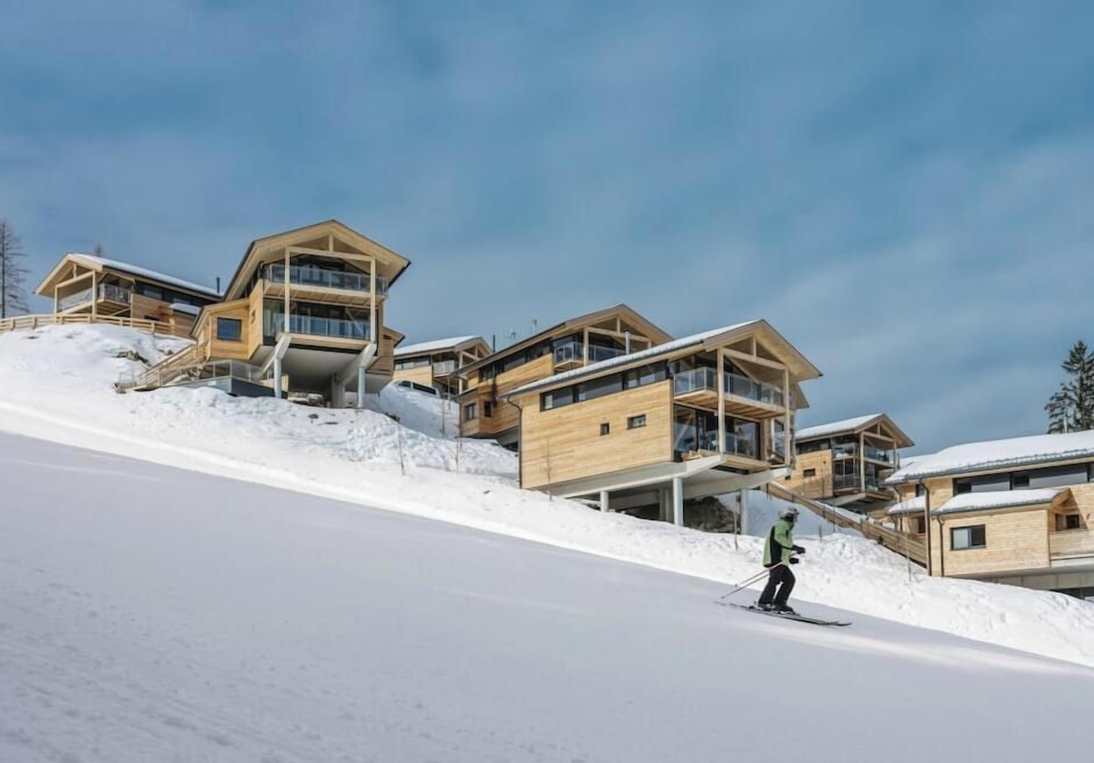 A ski resort with modern wooden buildings, a ski slope, and a skier.