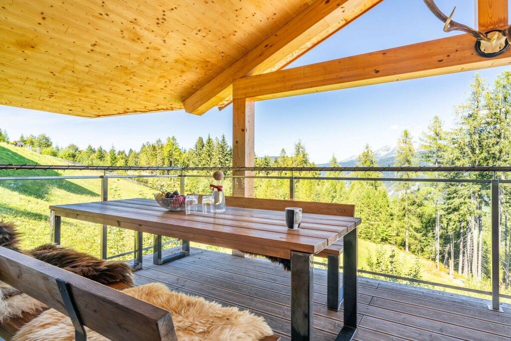 An outdoor wooden deck with a table and benches, overlooking a forested hillside.