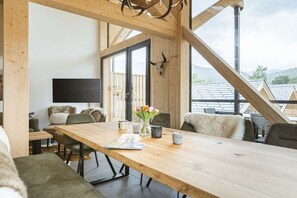 A modern interior with a wooden dining table, comfortable seating, a flat-screen TV, and a large window offering a view of the surrounding area. - Apartment with 1 bedroom (St. Georgen am Kreischberg)
