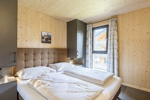 A room with a wooden ceiling and walls, a bed with white bedding, a mounted picture of a bull, and a window with curtains. - Apartment with 1 bedroom (St. Georgen am Kreischberg)
