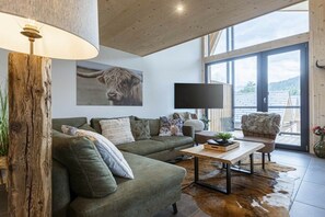 Un salon moderne avec un canapé vert, une table basse en bois et une grande fenêtre donnant sur l’extérieur.