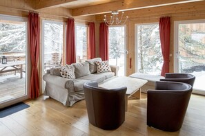 Interior acollidor d'una cabana amb seients de sofà, una taula de dinar i vista a un balcó cobert de neu.