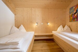A room with wooden walls, two beds with white bedding, and two wall-mounted lights. - Cabin in Turrach with sauna and Wi-Fi (Turrach)
