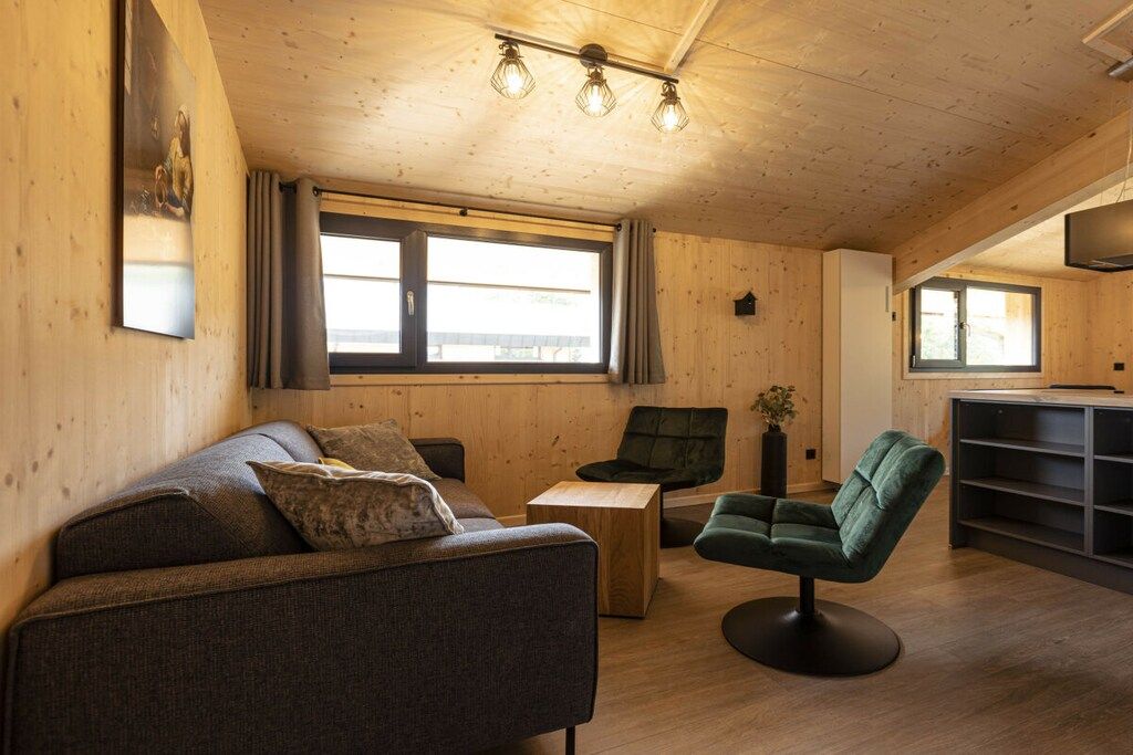 Ein gemütliches Zimmer mit einer Couch, einem grünen Sessel, einem kleinen Tisch und einem Fernseher auf einem Schrank.