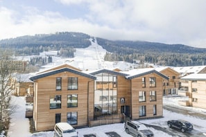 A modern building with a wooden facade, large windows, and a ski slope in the background. - Apartment with 1 bedroom (St. Georgen am Kreischberg)