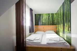 Ein Einzelbett mit Holzgestell, weißen Laken und einer Wandmalerei zum Thema Wald.