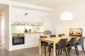 Une cuisine moderne avec des meubles blancs, un four encastré et un coin repas comprenant une table et des chaises en bois.