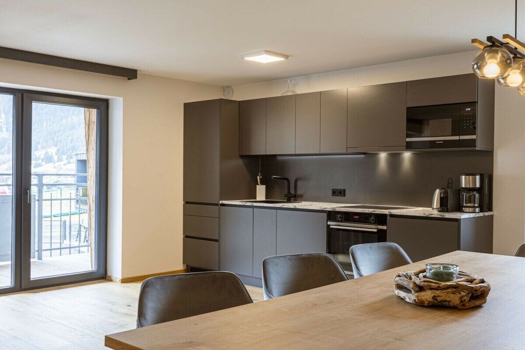 A modern kitchen with dark cabinetry, a central island, and a dining area with a table and chairs.