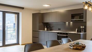A modern kitchen with dark cabinetry, a central island, and a dining area with a table and chairs.