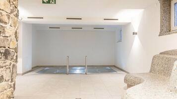 A swimming pool area with a stone wall, a tiled floor, and a mosaic chair.