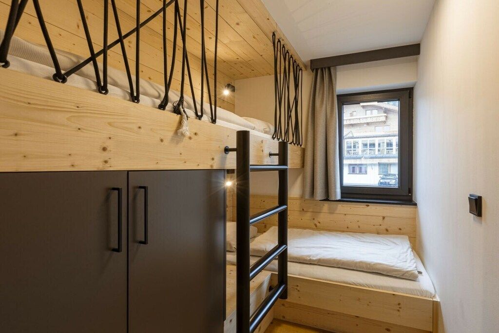 A bunk bed with a ladder, a wardrobe, and a window with a view of buildings.