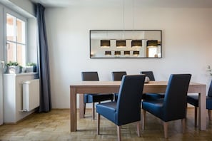 A dining area with a wooden table and six chairs, a large mirror on the wall, and a window with curtains. - Holiday apartment # 8 with balcony (Turrach)