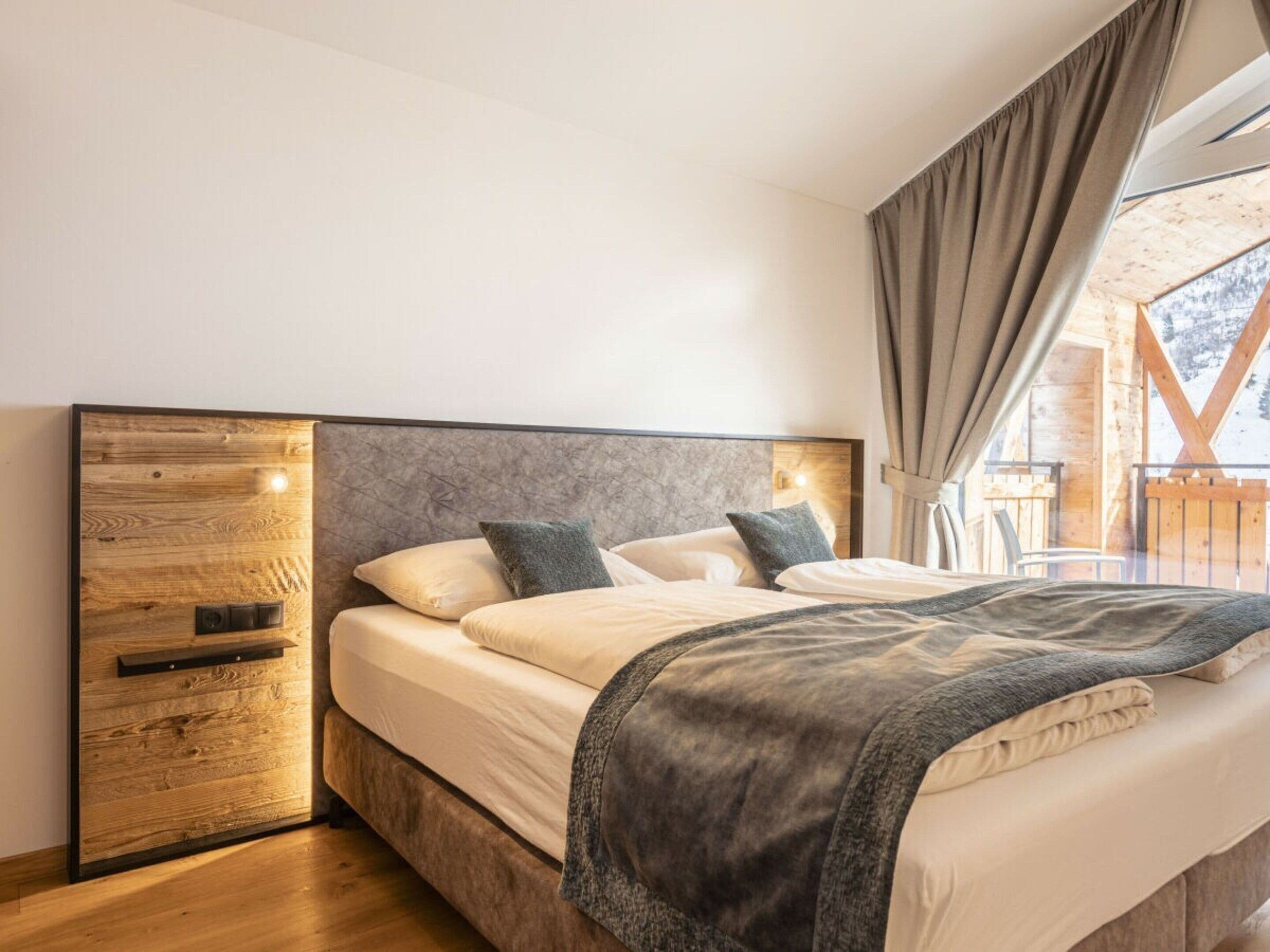 A bedroom with a wooden headboard, a bed with white bedding, and a view of a wooden deck outside.