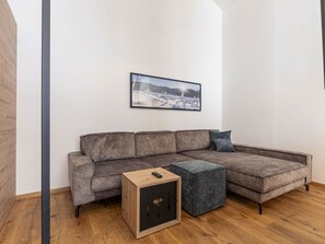 Ein modernes Wohnzimmer mit einer Eckcouch, einem kleinen Holztisch und einem grauen Hocker.