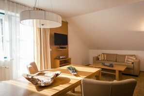 Ein modernes Wohnzimmer mit einem Holzesstisch, einer Couch, einem Fernseher und einem großen Fenster mit Vorhängen.