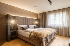 Ein modernes Schlafzimmer mit einem großen Bett, einem Kopfteil mit integrierter Beleuchtung und Blick ins Freie durch transparente Vorhänge.