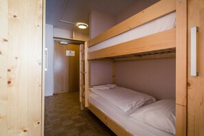 Quarto com beliches, piso de madeira e uma porta ao fundo.