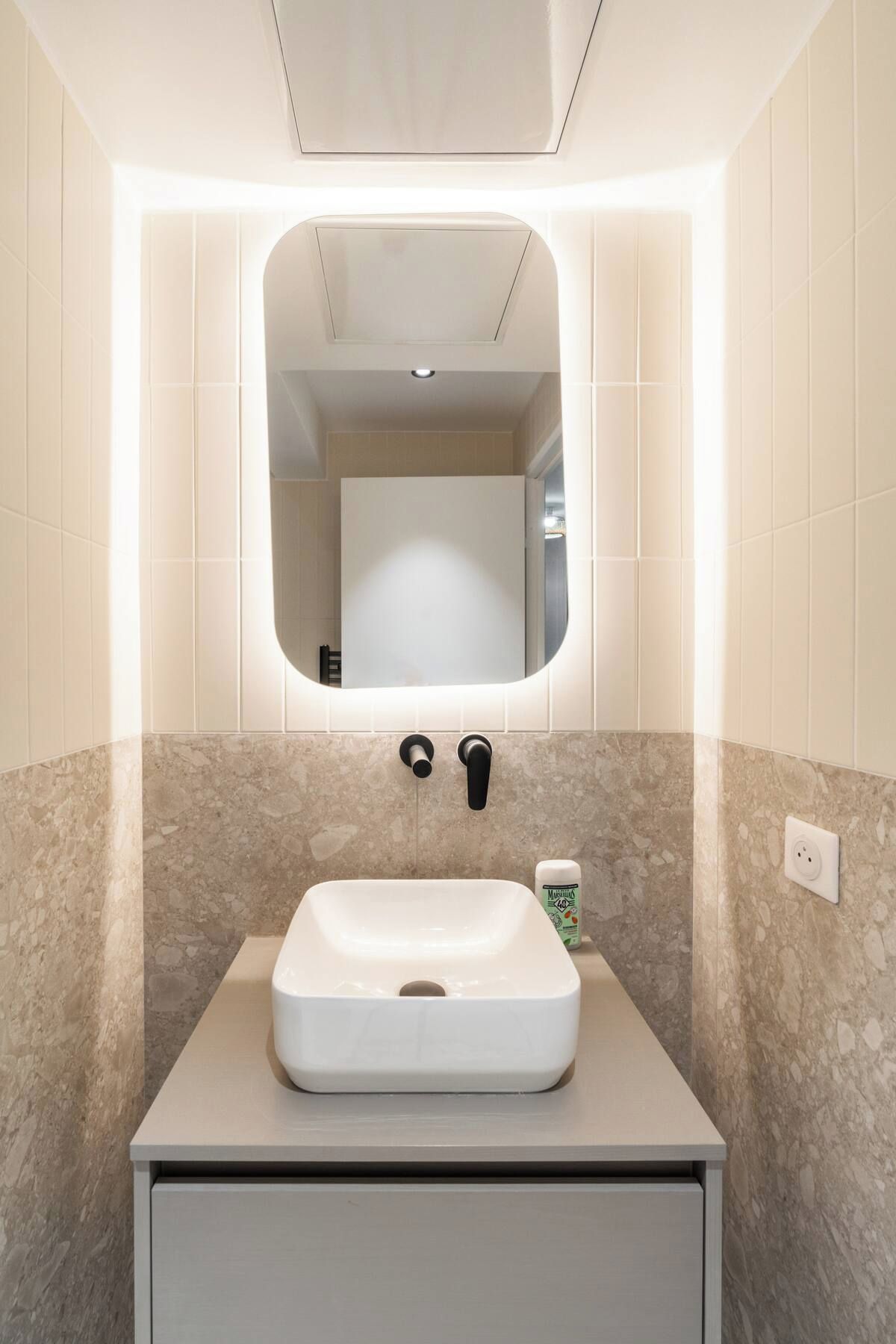 Ein Badezimmer mit einem weißen Waschbecken, einem Spiegel und einer Marmor-Spritzschutzwand.