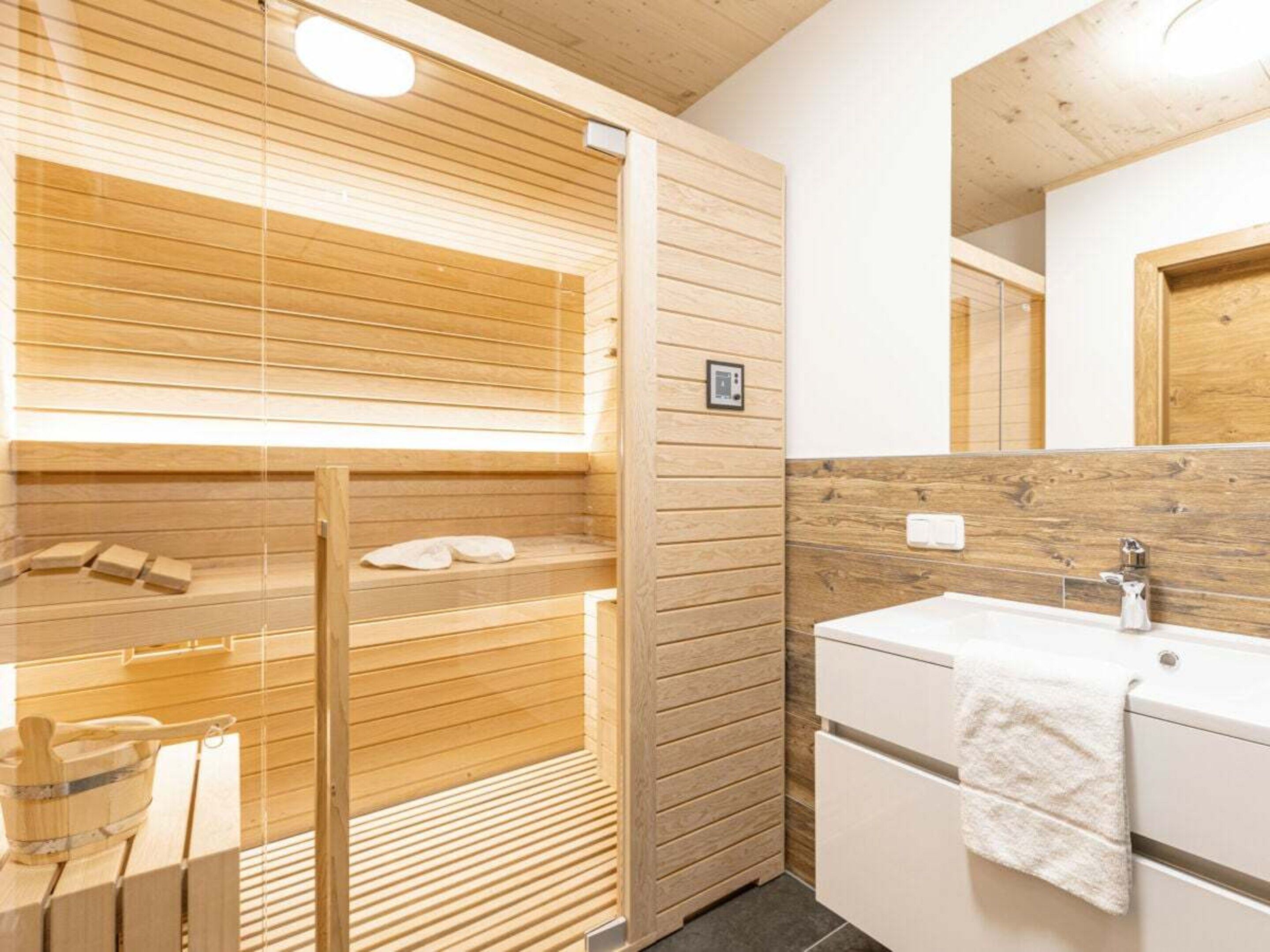 A modern bathroom with a wooden sauna, a sink, and a mirror.