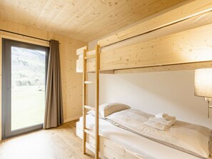 Ein Schlafraum mit Etagenbetten, Holzbalkendecke und einer Schiebetür zu einem Außenbereich.