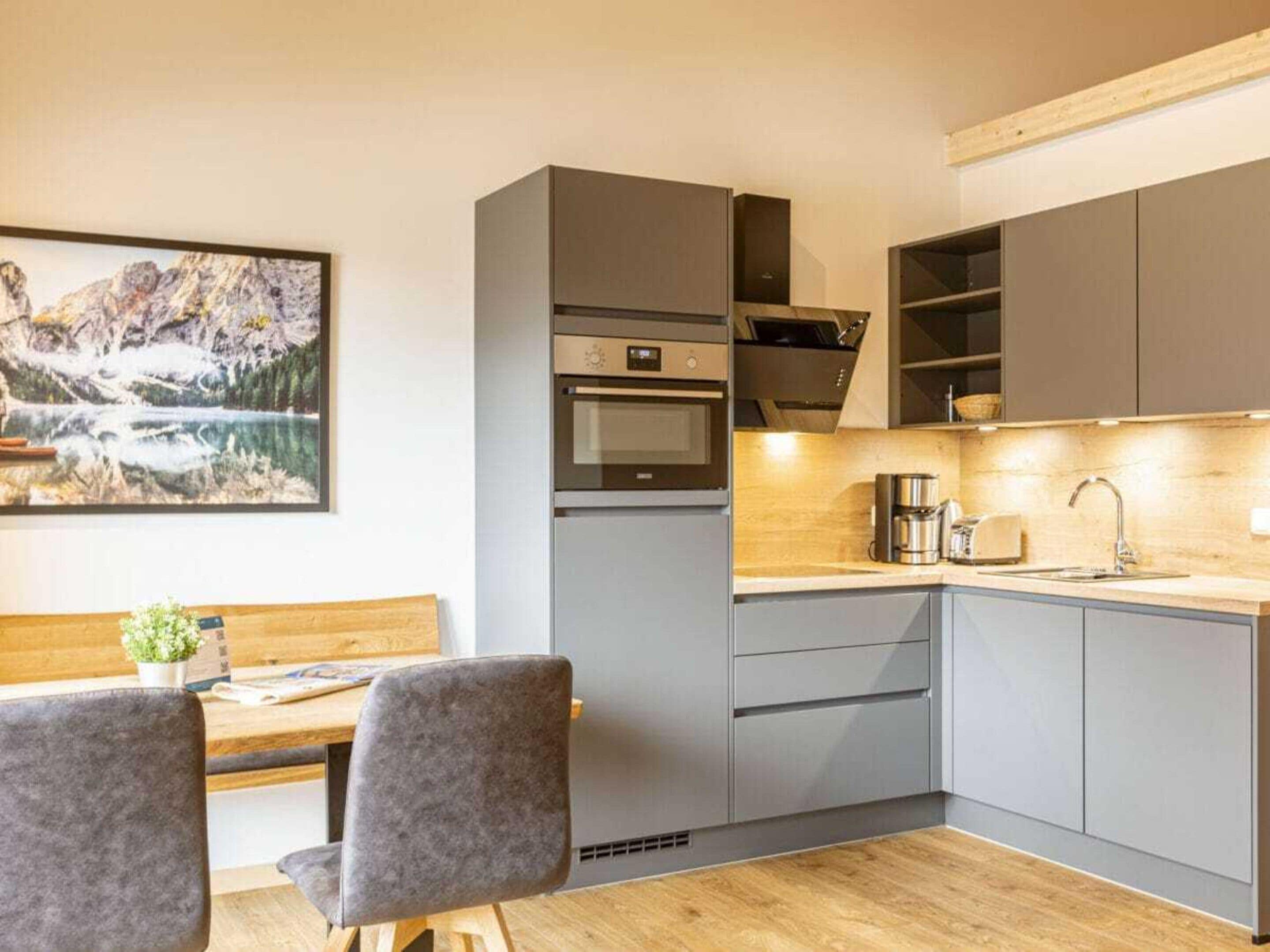Une cuisine moderne avec des meubles gris, un four encastré et un plan de travail en bois.
