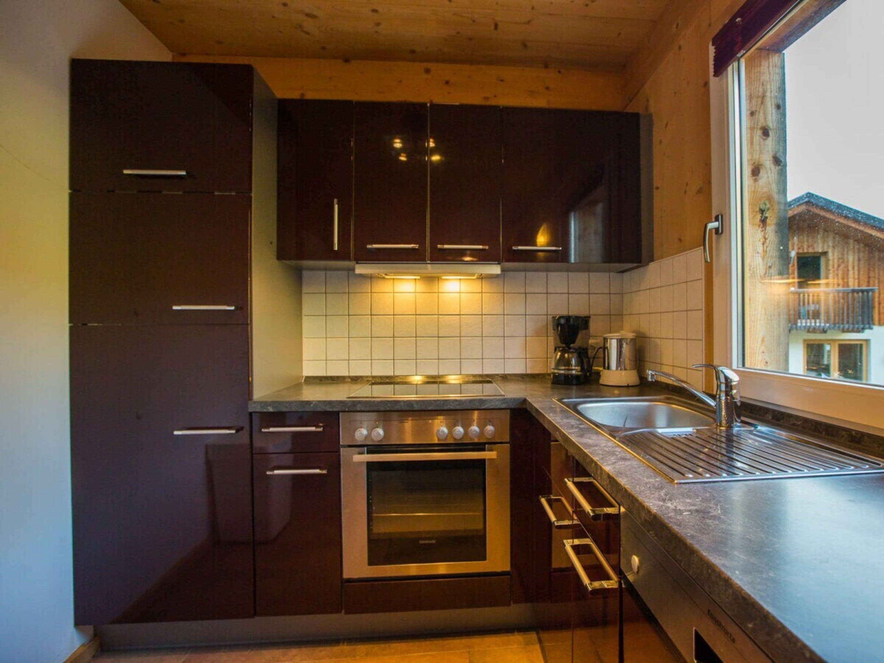 A modern kitchen with dark cabinetry, a stainless steel oven, a coffee maker, and a window with a view of a building.