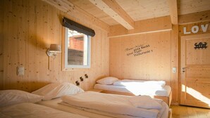 Een houten kamer met drie bedden, een raam met gordijn en een muur met een bericht.