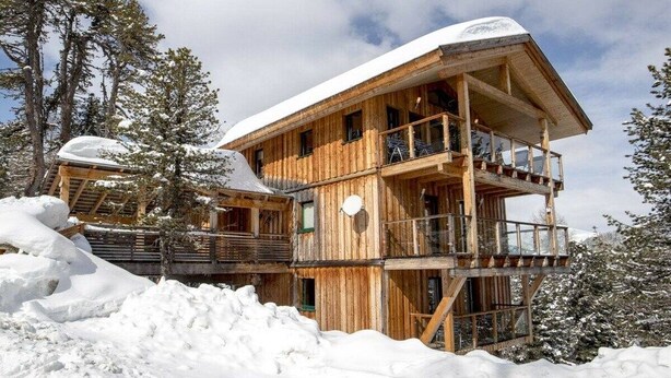 Een meerlaags houten vakantiehuis met balkons, omgeven door met sneeuw bedekte bomen.