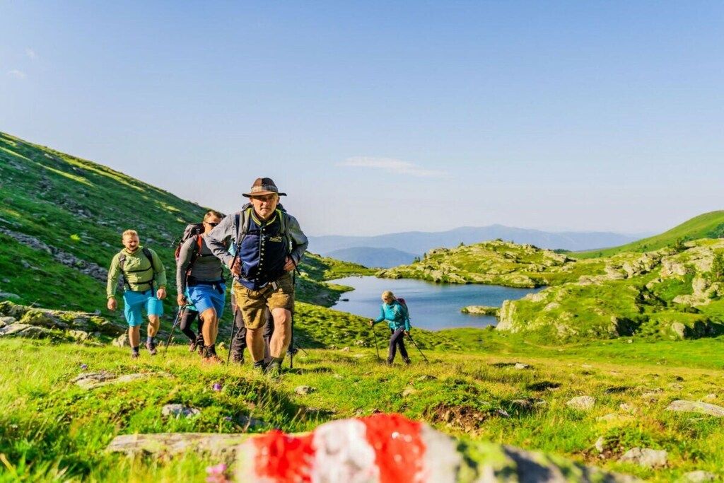 A group of hikers on a grassy trail with a lake and mountains in the background.