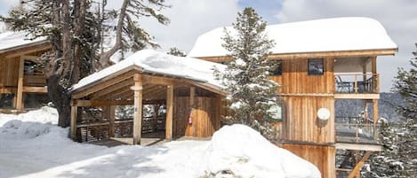 Un chalet en bois doté d’un porche couvert et d’un balcon, entouré de neige et d’arbres.