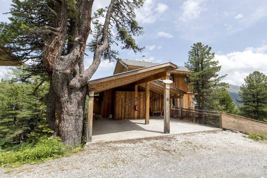 Een houten chalet met een overdekte veranda, omringd door bomen.